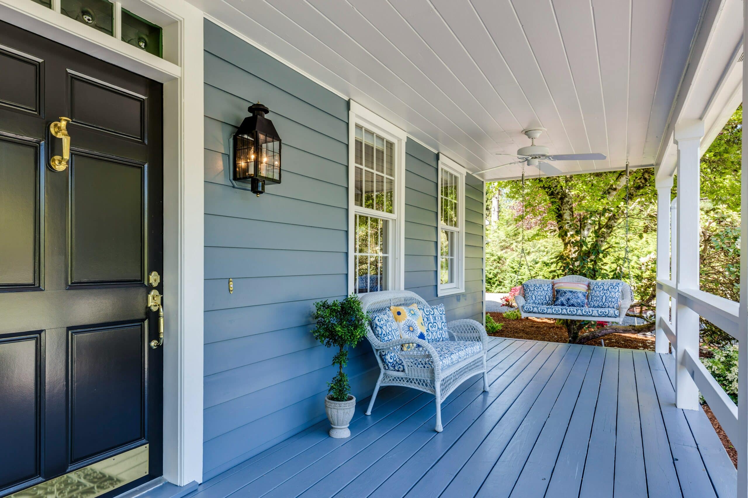 Welcoming porch with blue siding, painted deck, white wicker chair, and swing.